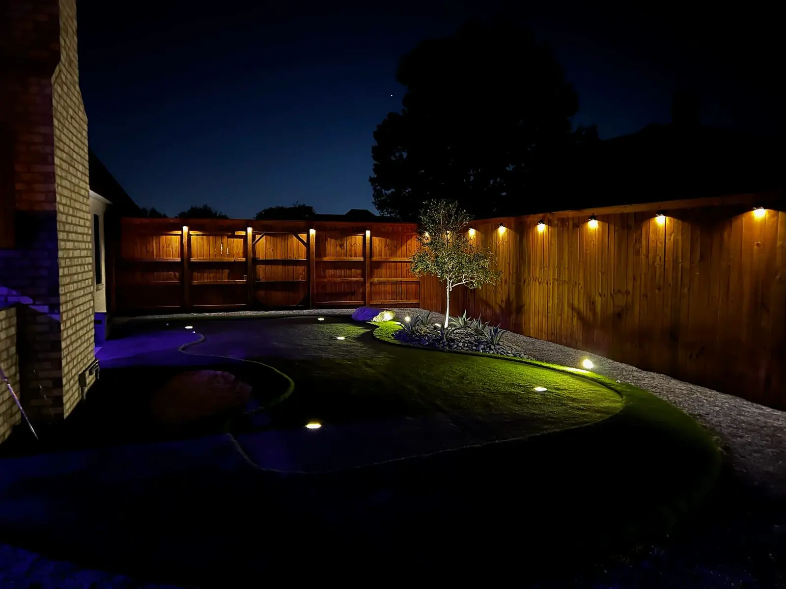 Pergola with string lights over a fireplace and an artificial turf yard